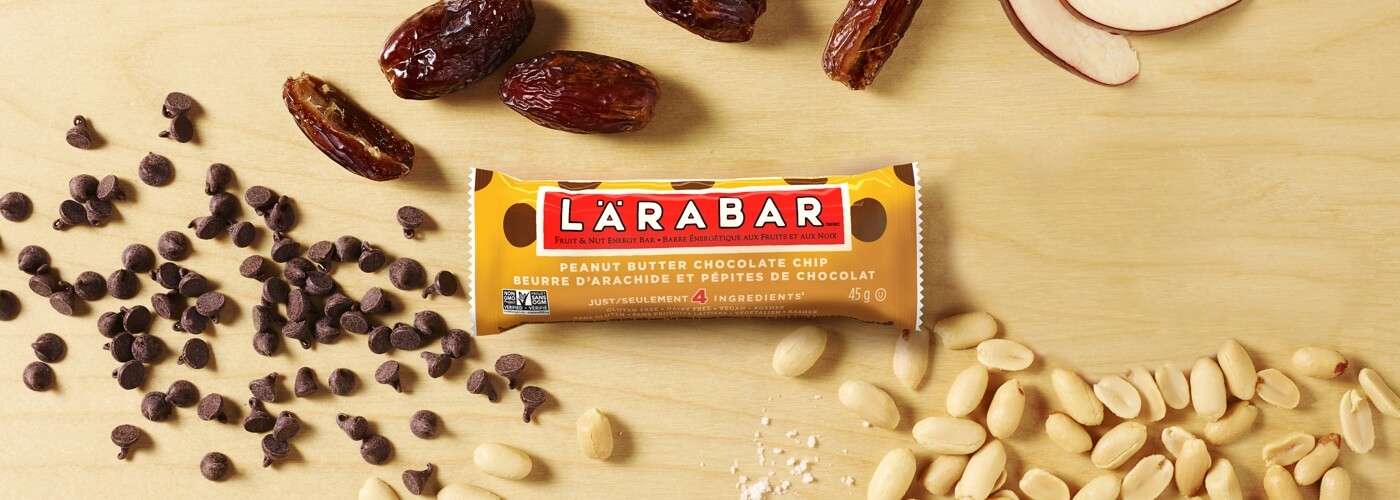 Lärabar sur une surface en bois avec des dattes, des arachides et des pépites de chocolat disposées à côté