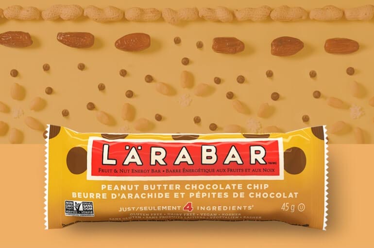 A Peanut Butter Chocolate Chip Larabar sitting against a backdrop of dates, peanuts, and coconut chips