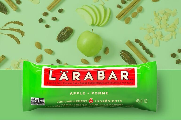 An Apple Larabar sitting against a backdrop of dates, almonds, apples, and cinnamon