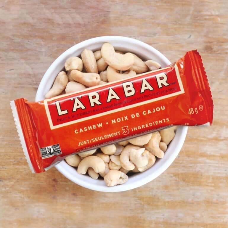 A red single pack of Cashew Larabar sitting in a cup of nuts