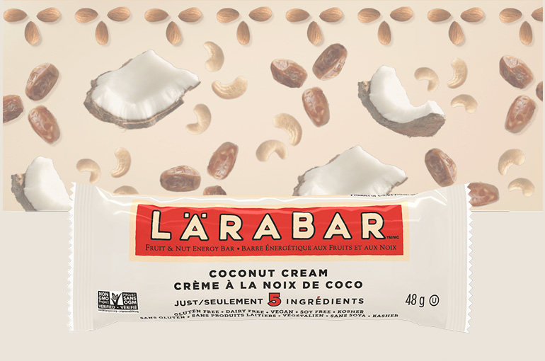 A Coconut Cream Larabar sitting against a backdrop of dates, cashews, and coconut chunks